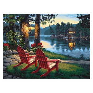 Diamond painting kit featuring a cozy cabin nestled near a lake with majestic mountains in the background.