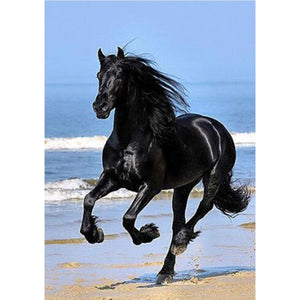 Diamond painting of a black horse gallops across a beach, kicking up sand as the waves roll in.