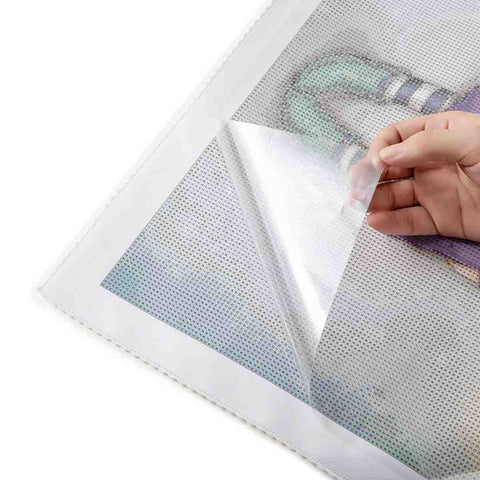 Image of Hand revealing the sticky surface of a diamond painting canvas by peeling back the protective film, preparing for the placement of diamond resins