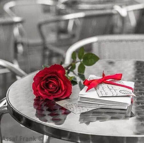 Image of Diamond painting of a red rose with a red ribbon on a table.